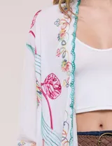 Kimono de poliéster blanco con diseño abierto, mangas amplias y bordados coloridos de motivos florales y arabescos, con terminaciones en ondas de hilo verde.