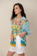 Camisa de manga larga con estampado tropical, fondo a rayas celestes y blancas, cuello camisero y cierre frontal de botones.