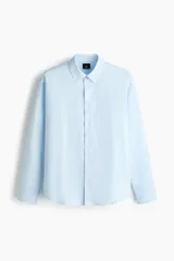 Camisa en mezcla de lino y algodón color celeste, de corte relajado, manga larga, con cuello inglés, bolsillo frontal y cierre de botones.