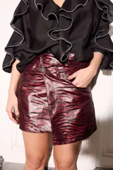 Blusa fluida color negro de corte holgado, con cuello alto, mangas largas y llamativos volados en cascada que recorren el frente y las mangas, decorados con costuras en hilo blanco en los bordes.