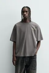 Camiseta de manga corta y cuello redondo, color gris oscuro con efecto lavado. Presenta un pequeño estampado en el pecho con texto en color verde lima.