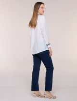 Camisa de crepe liviana y texturada color blanco, de silueta relajada y holgada, con cuello camisero clásico y puños con detalles de bordado de pasamanería con terminación deshilachada y aplique de perlas. Cuenta con cartera de botones oculta al frente y mangas largas.