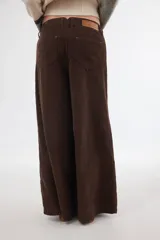 Pantalón sastrero de tiro medio confeccionado en pana de algodón. Presenta un diseño de pierna ancha con costuras verticales decorativas, bolsillos delanteros y traseros, y un detalle de aplique con ojalillo metálico en el ruedo de una de las piernas.