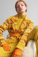 Saco largo medio con abertura frontal, bolsillos delanteros y cinto para ajustar. Presenta un diseño tejido con patrón geométrico en tonos amarillo, marrón y lila.