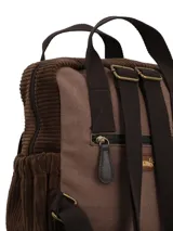 Mochila marrón de diseño patchwork y estilo bohemio, confeccionada en material textil. Cuenta con compartimento principal con cierre, bolsillo frontal con solapa decorada con tapicería estampada, bolsillos laterales, asas superiores fijas y correas ajustables. Incluye un llavero colgante lateral con borla y cuentas decorativas.