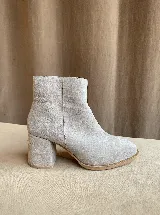 Botas de caña alta desmontables que se transforman en botinetas, confeccionadas en gamuza color beige. Presentan un diseño de punta semicuaadrada, taco cuadrado de 6 cm y detalle de estribo con hebilla forrada en el tobillo.