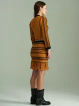 Top tejido de punto color mostaza con rayas horizontales en verde y rojo. Presenta cuello redondo, mangas largas ajustadas, hombreras y un corset integrado con rayas verticales en verde.