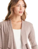 Cardigan de tejido liviano en color beige, con frente abierto y solapas tipo cascada. Presenta mangas largas entalladas con puños de rib y detalle de botones en la espalda.