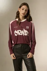 Remera de manga larga estilo deportivo, confeccionada en tejido técnico. Presenta un diseño color block en tonos bordó y rosa, con cuello mao y estampado gráfico frontal en color blanco.