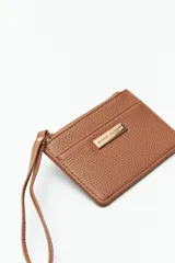 Billetera color mostaza con textura granulada, cierre superior con cremallera y correa de muñeca.
