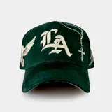 Gorra tipo baseball color verde, con bordado frontal de las letras 'LA' en tipografía gótica y una paloma blanca en el lateral. Cuenta con cierre ajustable en la parte posterior.