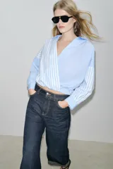 Camisa de popelín con estampado de rayas azules y blancas en diferentes direcciones, cuello solapa, escote pico cruzado, manga larga y bajo elástico.