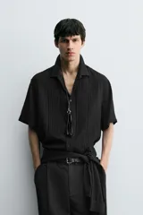 Camisa de corte relajado confeccionada en tejido fluido con textura acanalada. Presenta cuello solapa, manga corta y cierre frontal con botones.