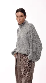 Sweater de punto grueso con cuello alto y mangas amplias de diseño holgado. Presenta costuras visibles en los hombros y puños acanalados.