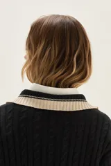 Sweater de punto con diseño de ochos en color crudo, con cuello polo y tapeta de botones en contraste verde. Presenta bordado en el pecho, puños y ruedo acanalados con detalles de rayas en verde.