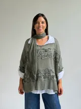 Sweater de punto color verde oliva con diseño de paneles horizontales de encaje floral, corte holgado y mangas tres cuartos. Incluye una bufanda del mismo tono y tejido, y se presenta superpuesto sobre una camisa blanca de cuello clásico.