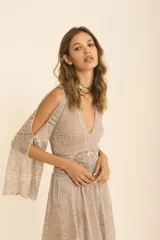 Vestido largo color champagne, con tejido de punto calado y textura brillante. Presenta escote en V, cintura marcada con frunces y mangas largas con abertura tipo capa.