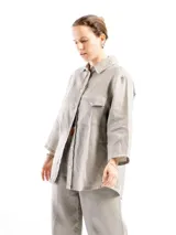 Camisa de lino con mangas tres cuartos, cuello clásico, cierre frontal con botones y un bolsillo en el pecho izquierdo. Presenta un diseño holgado con un pliegue en la espalda.