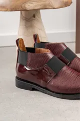 Bota corta color borgoña con textura de reptil, puntera fina, elástico negro en el empeine y talón descubierto.