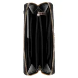 Billetera Guess modelo Lucci de color negro, confeccionada en material sintético con textura granulada. Presenta un cierre perimetral con cremallera y una tira de muñeca extraíble. En la parte frontal incluye el logotipo triangular característico de la marca con bordes dorados.