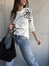 Remera blanca de manga larga con diseño de flor grande aplicada en relieve con cordón negro y blanco sobre el hombro izquierdo.