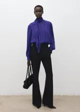 Blusa azul de manga larga con diseño texturizado a rayas verticales, cuello alto con lazada integrada y cierre frontal con botones revestidos.