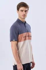 Remera polo de manga corta con diseño en bloques de color en tonos azul marino, blanco y verde militar, con bordado frontal y cierre de botones.