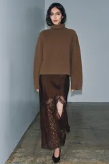 Falda midi de tiro alto confeccionada en tejido satinado color marrón. Presenta un diseño evasé con aplicación de encaje en el lateral y el bajo, y cierre lateral con cremallera oculta.