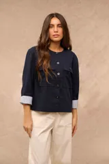 Campera azul marino de corte recto, con cuello redondo, cierre frontal con botones oscuros, bolsillos frontales con solapa en el pecho y mangas largas con vuelta estampada a rayas.