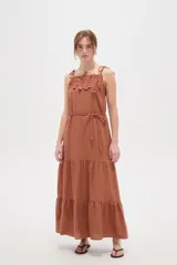 Vestido largo de algodón color tostado, de corte holgado, con cuello recto, breteles finos ajustables con lazo y falda con volados escalonados. Presenta apliques de flores bordadas en el pecho y un cordón ajustable en la cintura.