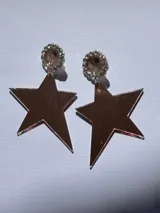 Caravanas colgantes con base redonda de resina negra rodeada de strass dorado, y dije en forma de estrella de acrílico espejado color cobre.