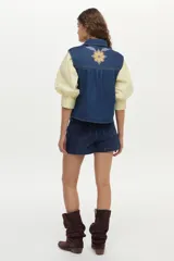 Chaleco de denim azul oscuro con cuello clásico y bordados florales en tonos amarillos, blancos y celestes en la parte delantera.