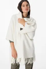 Ruana de tejido suave y envolvente en color blanco, con diseño de corte amplio y terminación de flecos en el ruedo.