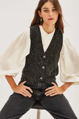 Chaleco de algodón negro con diseño de chaleco de vestir, cuello en V y cierre frontal con botones. La tela está completamente adornada con pequeños apliques brillantes que simulan un efecto de estrellas o puntos de luz.