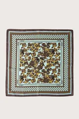 Pañuelo cuadrado con estampado central de manchas tipo animal print en tonos marrones y negros sobre fondo celeste, enmarcado por un borde geométrico con detalles en celeste, marrón y dorado.