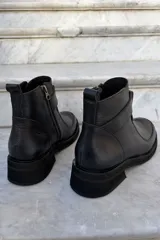 Bota corta de cuero negro con diseño de caña media, cierre lateral y detalle de tira horizontal sobre el empeine. Posee suela de goma gruesa y puntera redondeada.