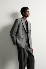 Blazer de corte relaxed fit color gris, confeccionado en tejido con lana. Cuenta con solapas de pico, manga larga con botones en los puños, bolsillos con solapa en la cadera y un bolsillo de vivo en el pecho. Presenta cierre frontal de botonadura cruzada con botones oscuros.
