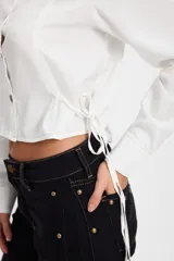 Camisa corta estilo corset de color blanco, con cuello clásico, cierre frontal de botones y detalles de cordones laterales ajustables. Presenta pinzas frontales y traseras para un ajuste entallado.