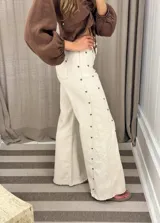Pantalón de pierna ancha con acabado brillante, confeccionado en lino. Presenta un diseño de tiro medio con cierre de botón y cremallera, bolsillos traseros y etiqueta de marca en la cintura.