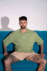 Remera oversize de algodón elastizado color verde militar, con cuello redondo, mangas cortas y diseño gráfico bordado en el pecho.