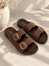Sandalias marrones de dos tiras con hebillas metálicas doradas, base de aspecto amaderado y plantilla plana.