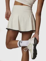 Conjunto deportivo compuesto por una musculosa blanca sin mangas con cuello alto y cierre frontal, y una pollera blanca con borde inferior en contraste negro.