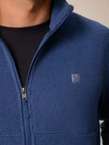 Campera de polar tipo sherpa en color azul, con cierre frontal completo, cuello alto y bolsillos laterales. Presenta un pequeño logo bordado en el pecho.