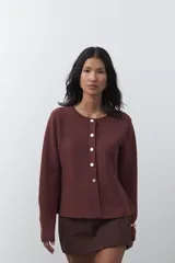 Cardigan negro de tejido de punto con cuello redondo y cierre frontal con botones a contraste. Presenta un corte entallado en la cintura con una silueta levemente evasé y mangas largas.