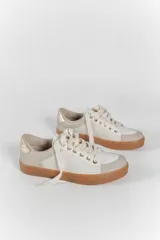 Zapatillas color marfil con detalles dorados en el talón y ojales metálicos. Suela de goma caramelo y cordones beige.