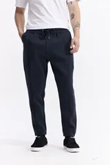 Pantalón de jogging negro de algodón y poliéster, con puños ajustados en los tobillos, cintura elástica con cordón y costuras verticales marcadas en el frente.