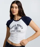 Remera de estilo college con cuerpo blanco y mangas raglán cortas en color azul marino. Presenta cuello redondo y estampa frontal con diseño gráfico deportivo de Santa Monica.