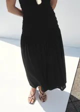 Vestido midi negro sin mangas, con cuello redondo, fruncidos en el cuerpo y falda de corte evasé.