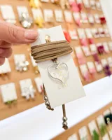 Choker de tiento de gamuza color beige, con dije de corazón plateado calado y terminales con cuentas metálicas esféricas.