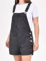 Monoprenda short de jean negro con efecto gastado, tirantes ajustables con hebillas metálicas y bolsillos frontales.